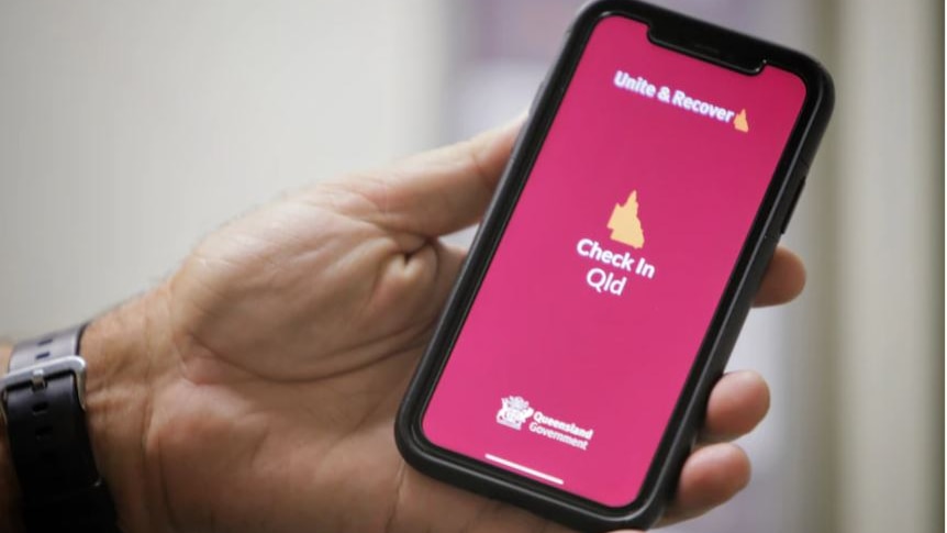 A hand holds a mobile phone, with the Check In Queensland app open.