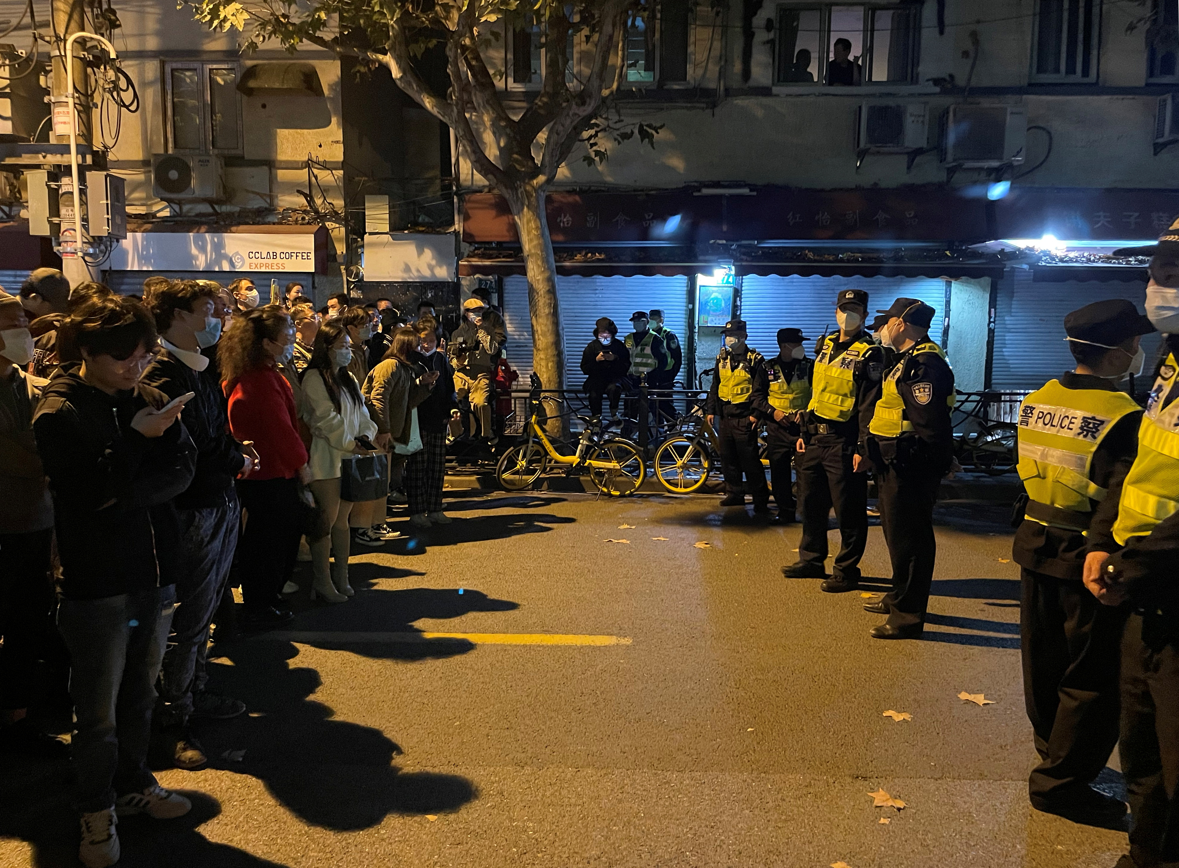 A group of people stand on one side of the street facing a group of police. 