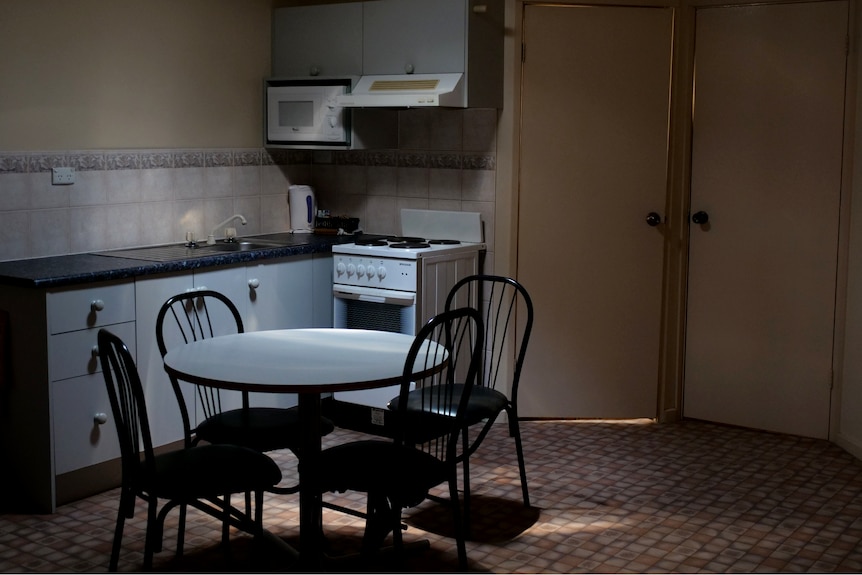 A table and chairs lit in a dark kitchen.