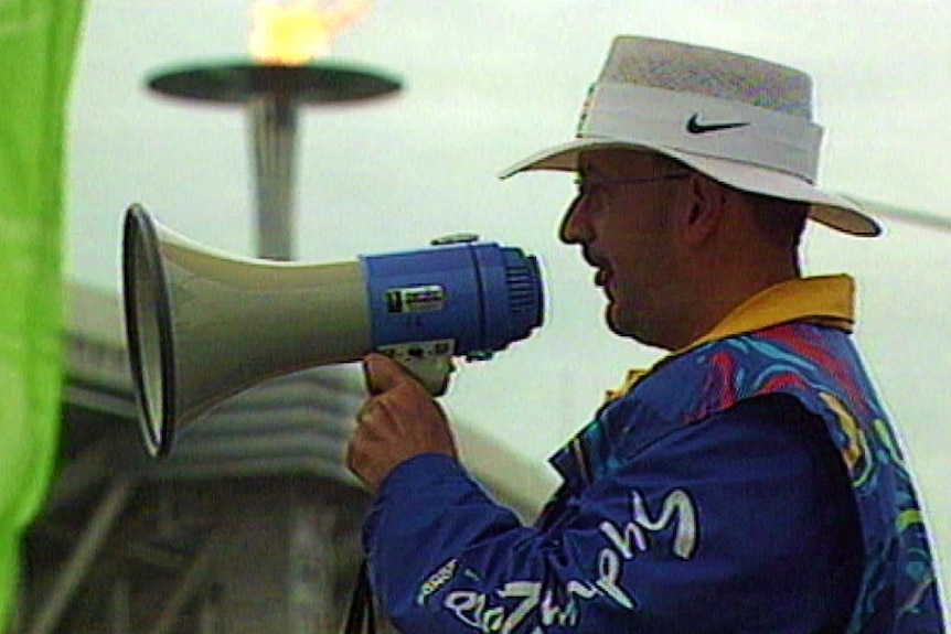 A Sydney Olympic volunteer speaks through a loud hailer, with the Olympic cauldron in the background.