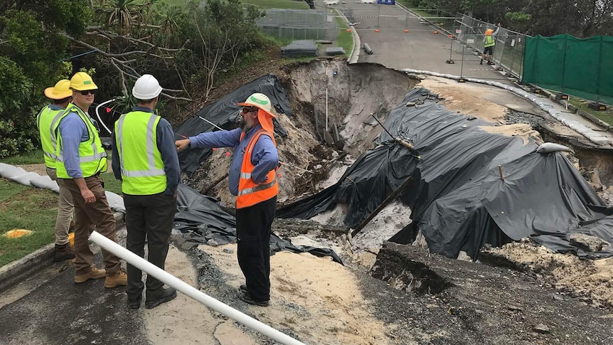 Men standing around a large road collapse at a beachside residential suburb