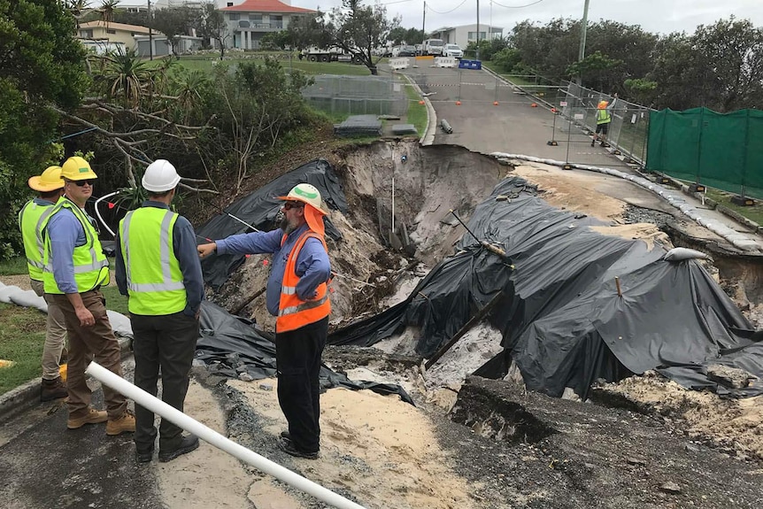 Men standing around a large road collapse at a beachside residential suburb