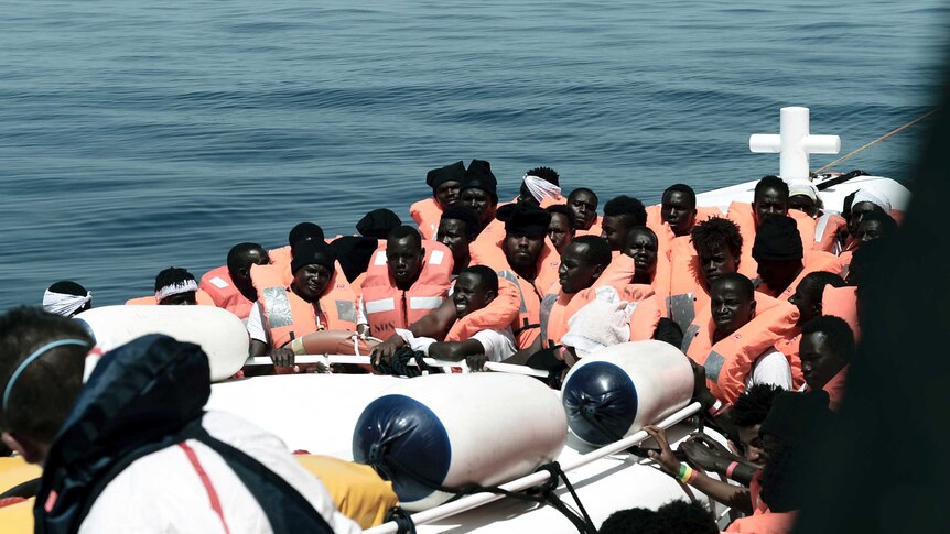 Migrants are seen crammed into a small boat, wearing orange life jackets