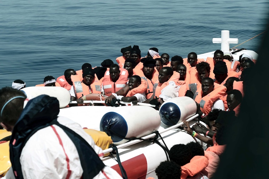 Migrants are seen crammed into a small boat, wearing orange life jackets