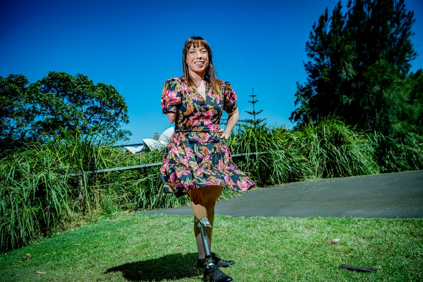 A smiling woman with a floral dress in the sunshine. She has a prosthetic leg