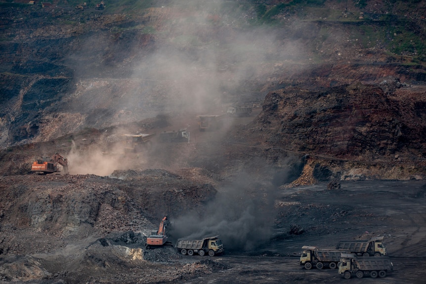 Open cut Indian coal mine in production with smoke billowing and trucks manouvering