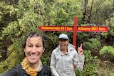 two people with trees behind them, smile and point to a sign post that says Kalamunda in one direction and Albany in the other 