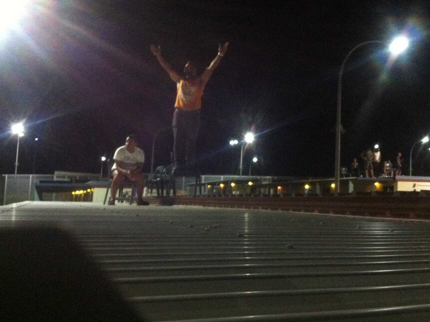 A protester stands on a roof with his arms raised.