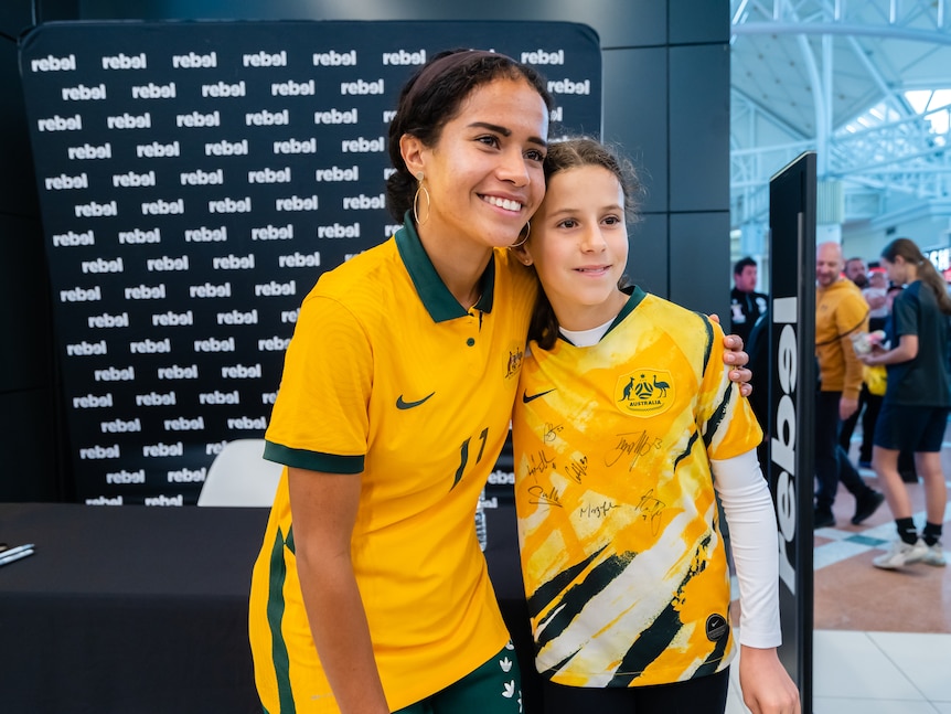 A female soccer player wearing yellow and green takes a photo with a fan