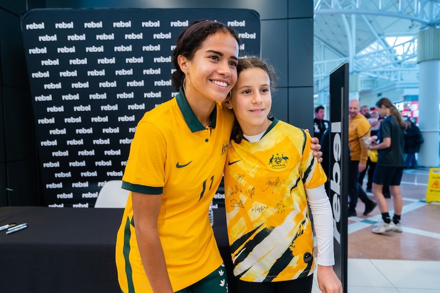 A female soccer player wearing yellow and green takes a photo with a fan