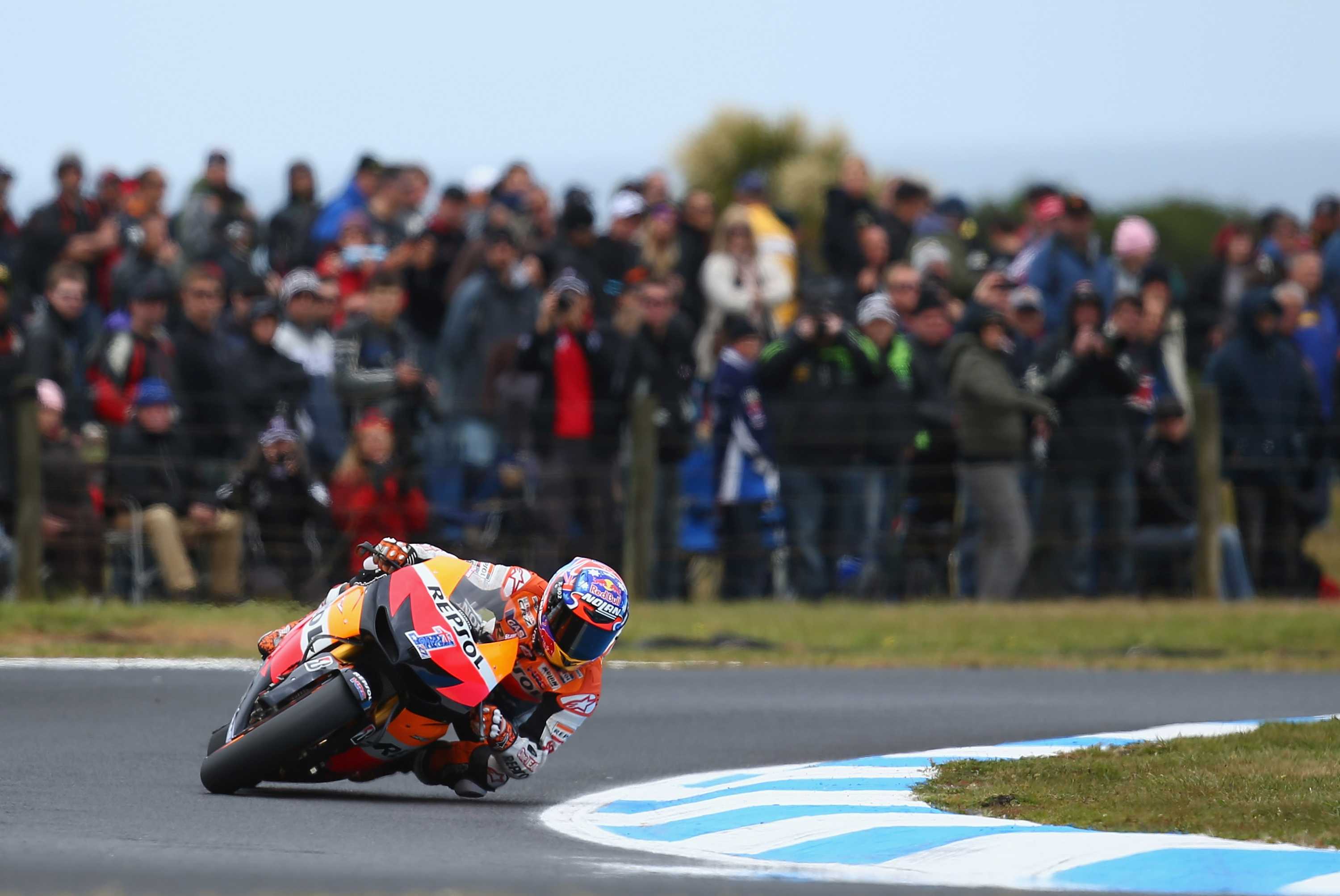 Um motociclista se inclina para uma curva durante uma corrida na frente de uma grande multidão.