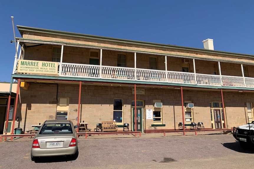 A two-storey building made of sandstone with several cars are parked in front.