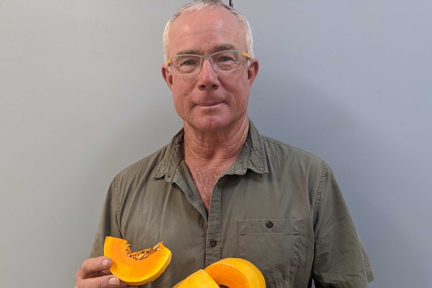 Shaun Jackson standing in front of a grey background holding the pumpkin variety he cultivated.