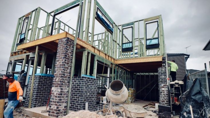 A double story house being build with timber frames at the top and a builder to the left and far right