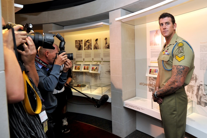 Several photographers point cameras at a man, who is standing, looking on.