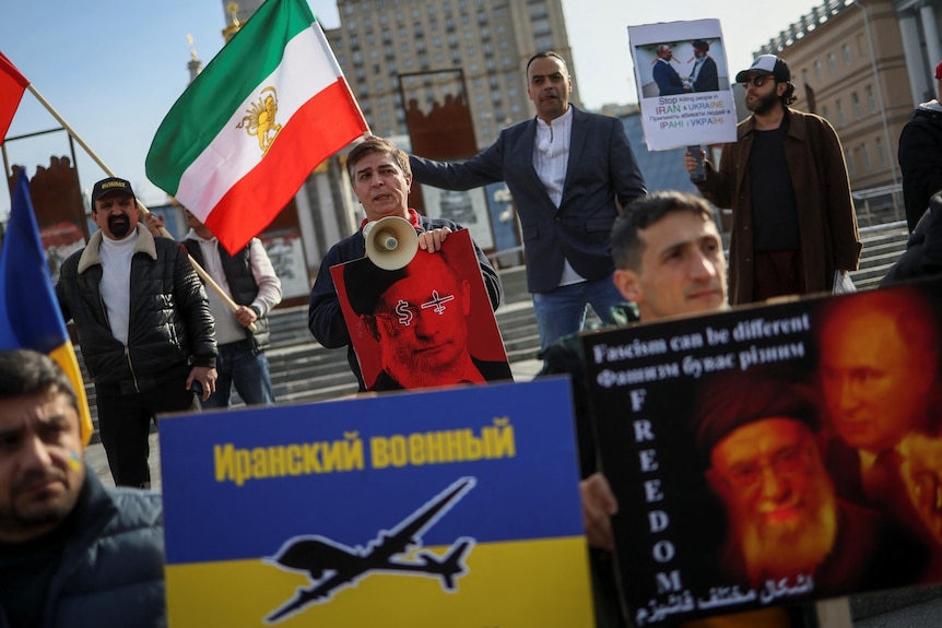 A group of protesters in the street holding Iranian flags and anti-drone signs. 