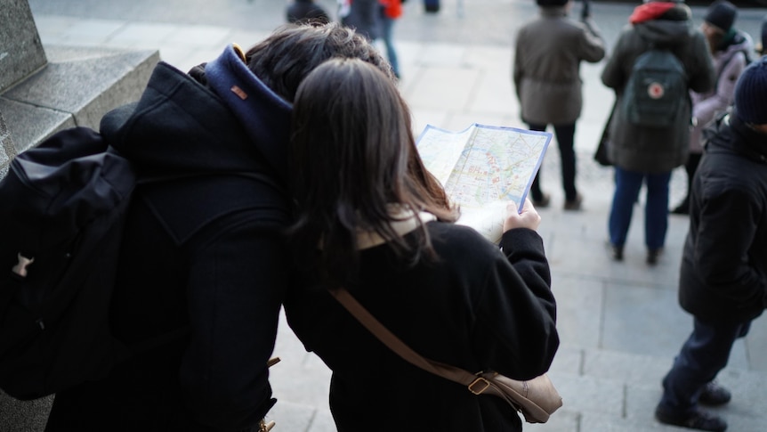Two tourists in coats look at a map. 