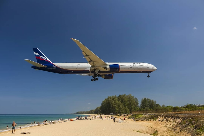 A plane flies in to land over people sunbathing and swimming at Mai Khao beach