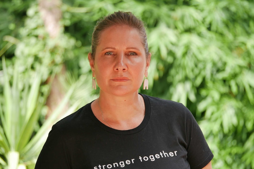 Stacey Ross from the Centre for Women wears a black shirt that says stronger together while standing in front of a tree.