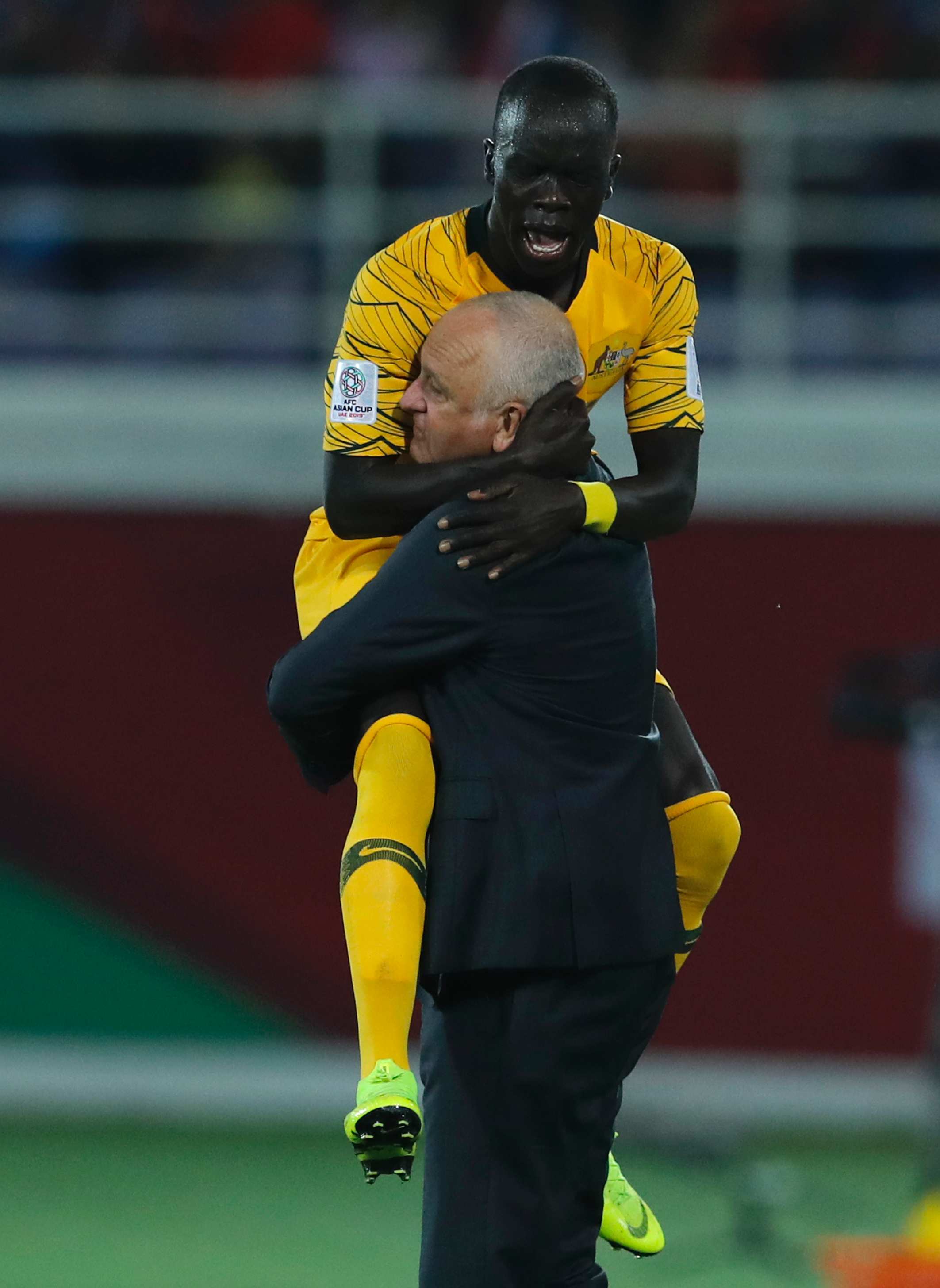 A socceroos player jumps on and celebrates with a soccer coach.