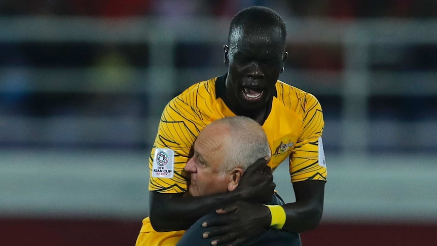 A socceroos player jumps on and celebrates with a soccer coach.