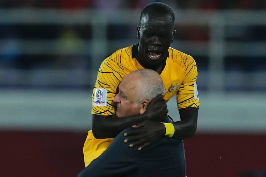 A socceroos player jumps on and celebrates with a soccer coach.