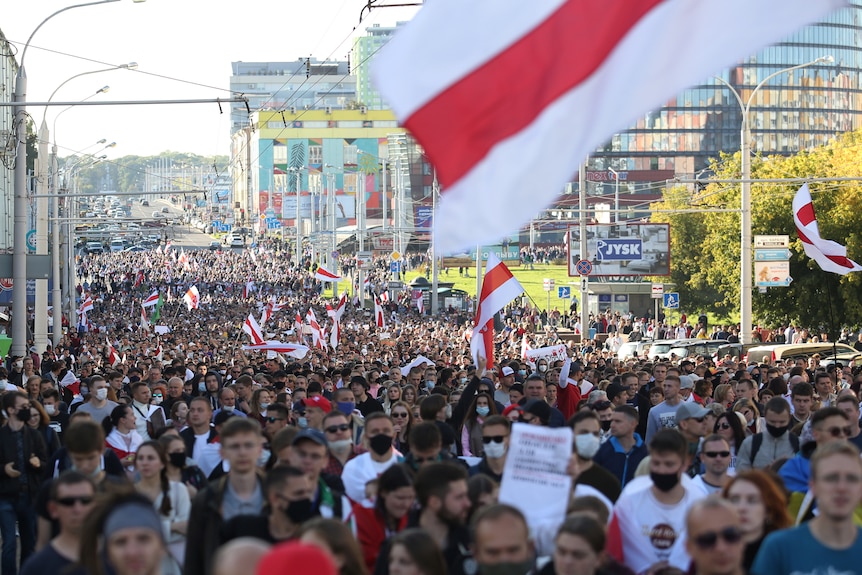 Looking down a street, hundreds of thousands of people march, holding red and white flags and placards