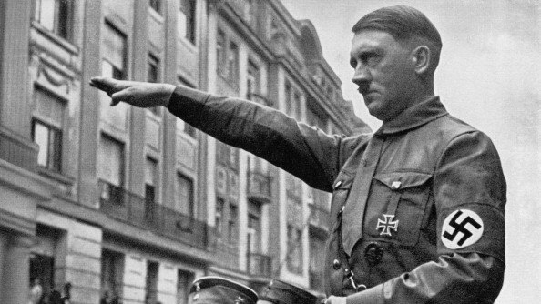 Adolf Hitler on the back of am open-air truck with his arm outstretched. Black and white.