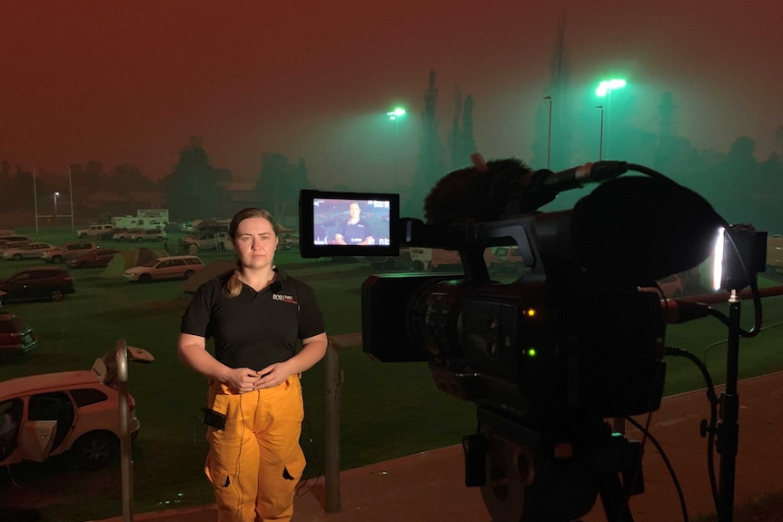 Reardon standing in front of camera with cars and tents in background under dark orange sky.