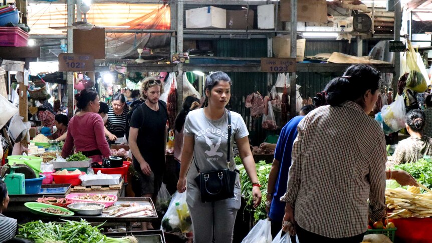 people crowd the walkways of a Cambodian marketplace filled with fruit and vegetables