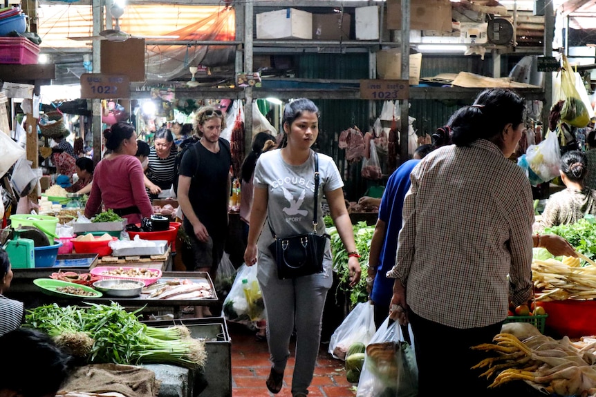 people crowd the walkways of a Cambodian marketplace filled with fruit and vegetables