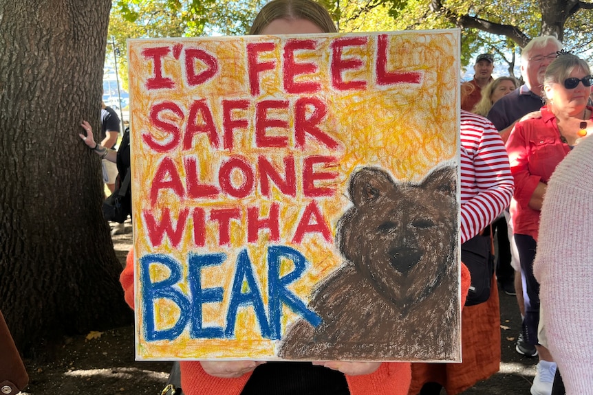A sign in front of a person's face that says 'I'd feel safer alone with a bear'