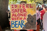 A sign in front of a person's face that says 'I'd feel safer alone with a bear'
