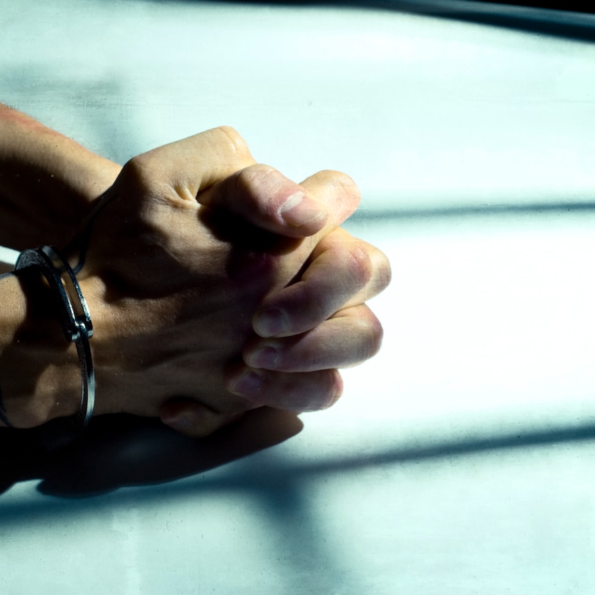 A man's handcuffed hands clasped while resting on a table.