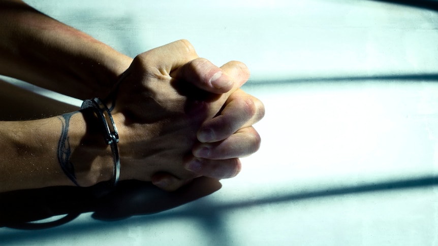 A man's handcuffed hands clasped while resting on a table.