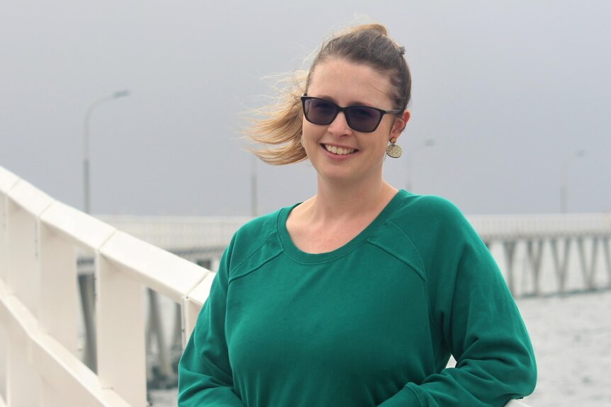She stands in a green jumper on the Esperance jetty on a rainy day