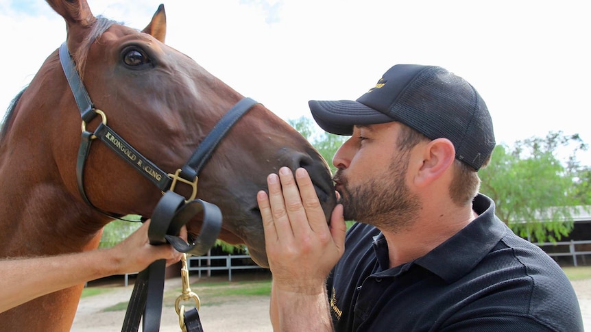 A man kisses a racehorse on the nose.