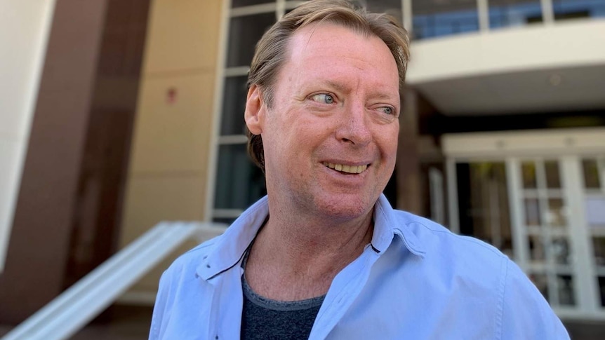 A man smiles outside a court.