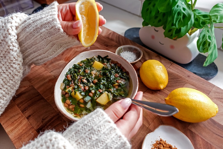 A hand squeezing lemon juice on top of a bowl of lentil potato and spinach soup.