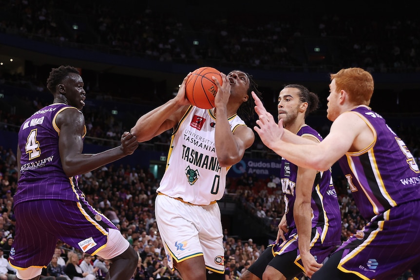 Un jugador de baloncesto con el balón se eleva por encima de cuatro defensores.