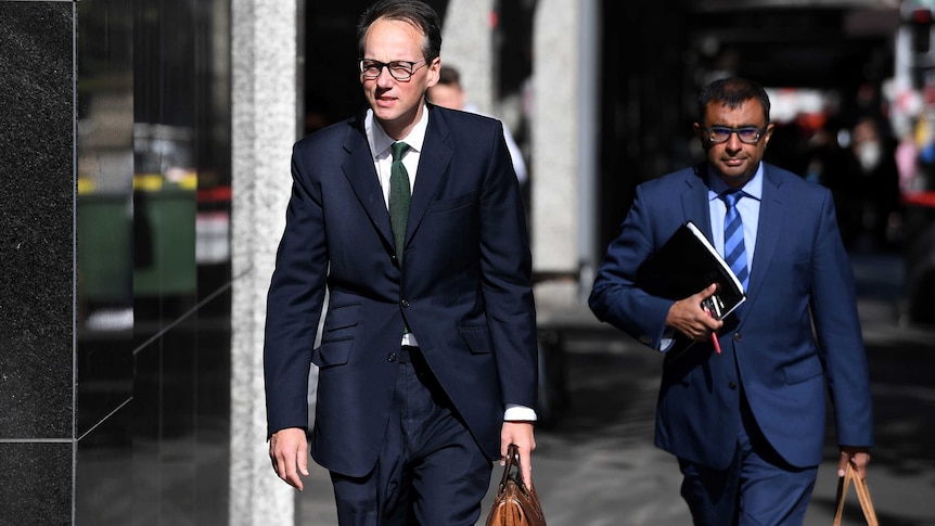 two men in suits with glasses walk on a footpath