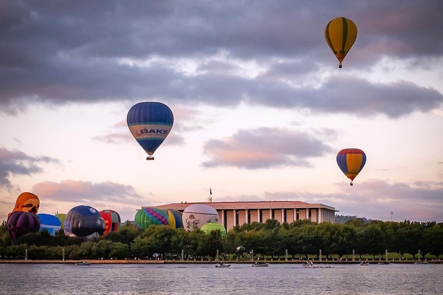 Hot air balloons above a lake on a cloudy morning.