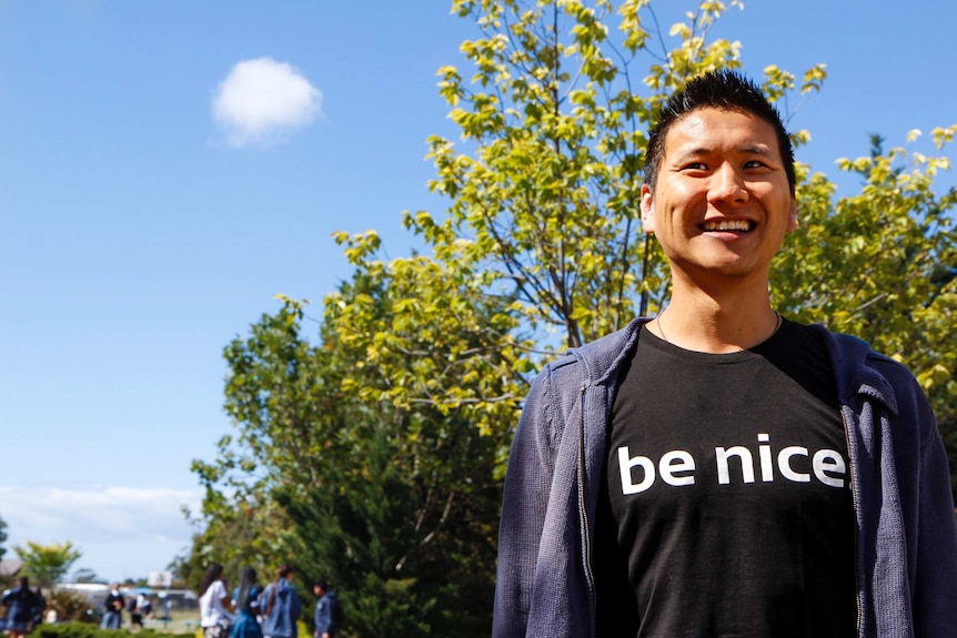 Vincent Shin stares into distance camera as students walk past in school grounds in background.