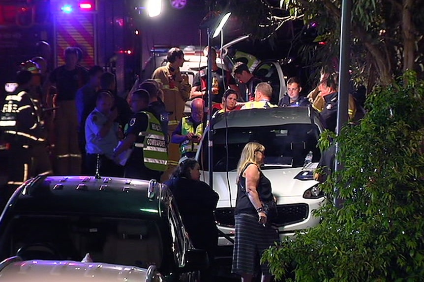 People including emergency service workers gather in a street.