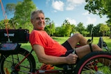 Posed shot of man in bright orange shirt on recumbent tricycle.