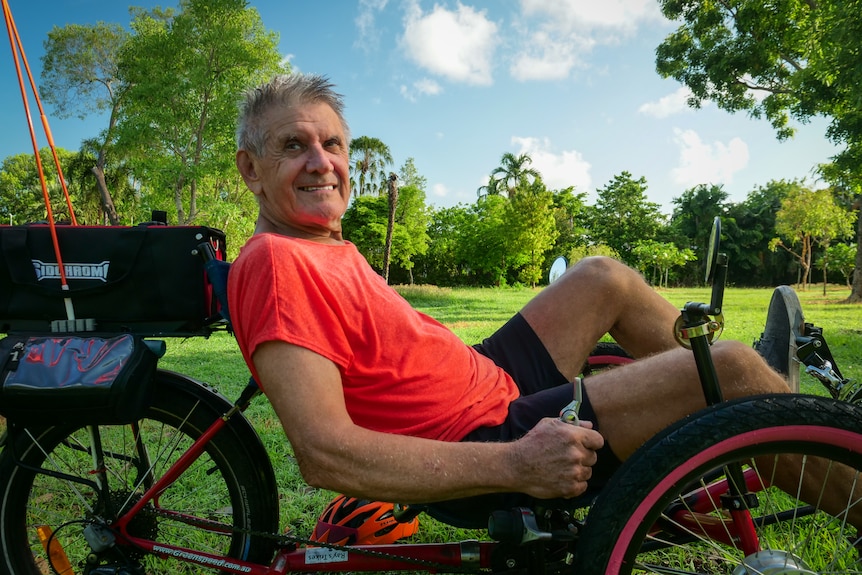 Posed shot of man in bright orange shirt on recumbent tricycle.