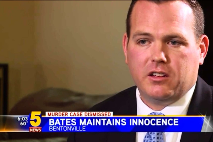 Man in suit sits in living room with TV news strap line underneath that reads "Bates Maintains Innocence"