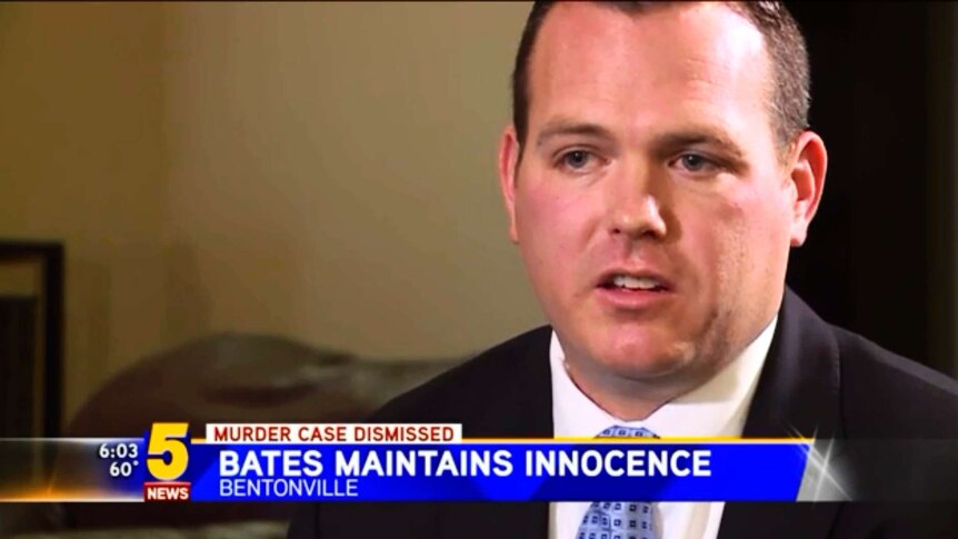 Man in suit sits in living room with TV news strap line underneath that reads "Bates Maintains Innocence"