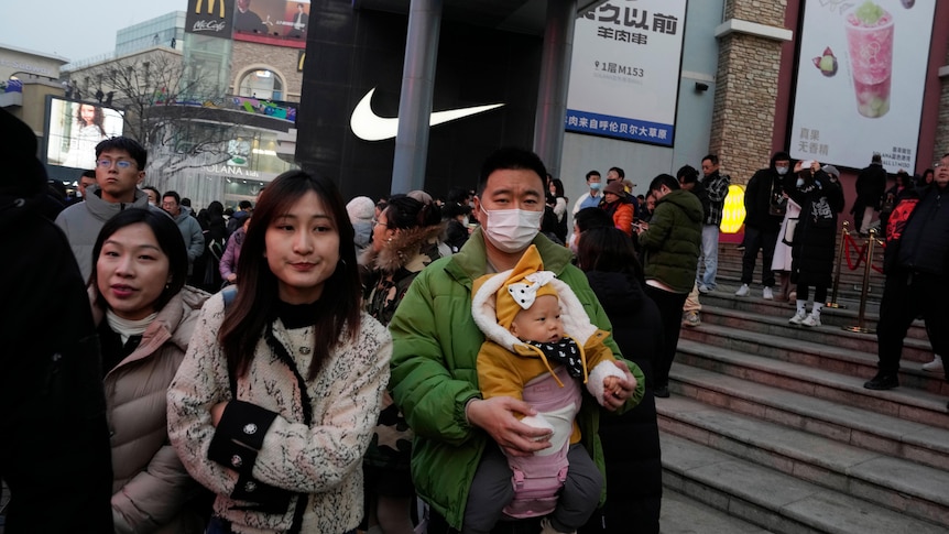 A Chinese man carries a child at a crowded shopping mall.