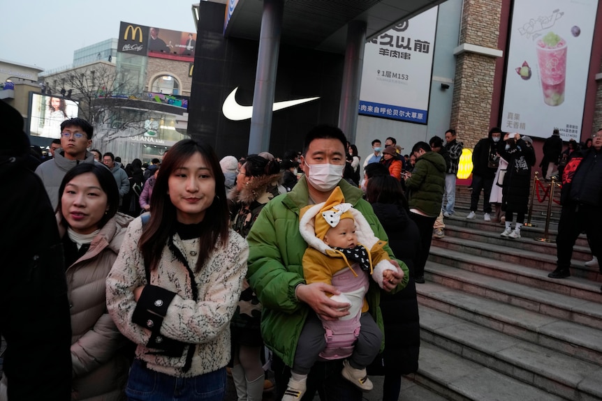 A Chinese man carries a child at a crowded shopping mall.
